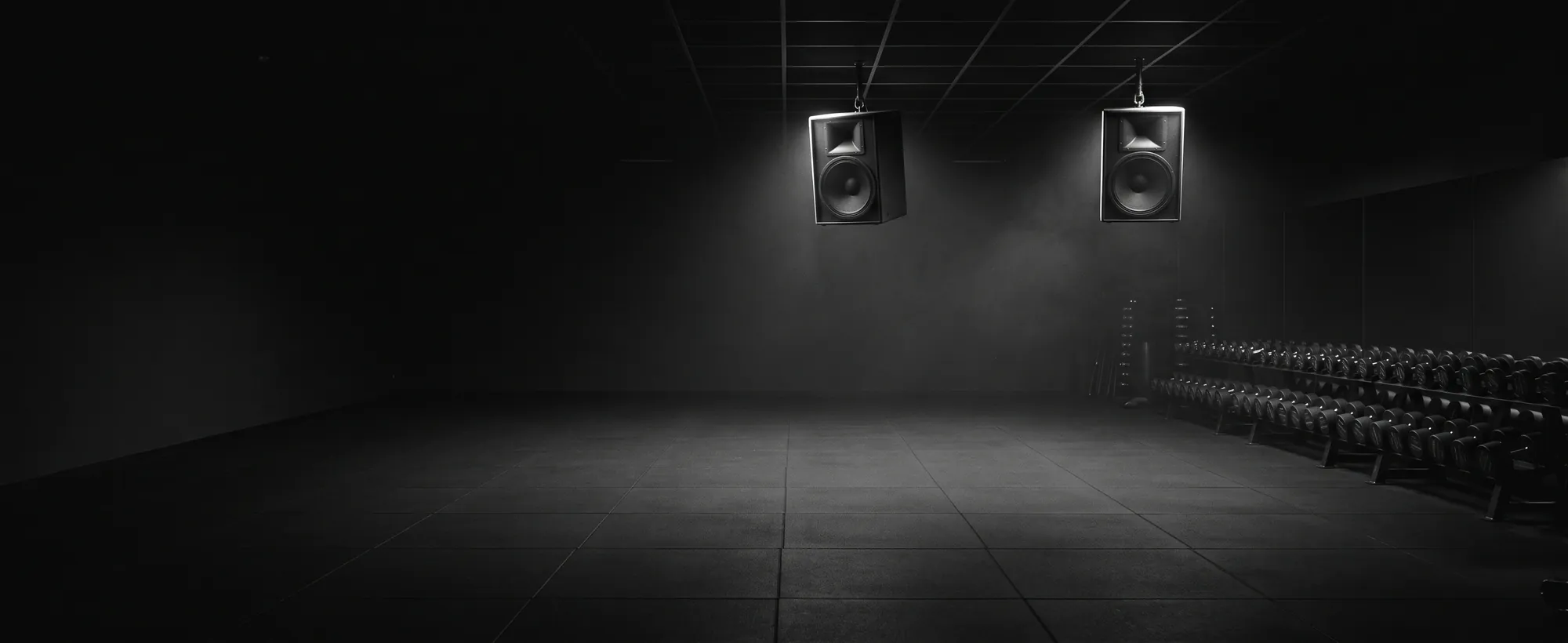 Commercial audio system installation for gyms and venues, South India. A gym floor at night with pendant-mounted loudspeakers catching a cool rim light.
